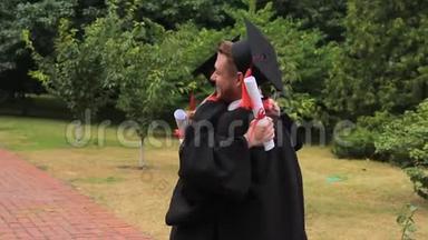 快乐的毕业生拿着毕业证书，在学院附近的公园拥抱，快乐